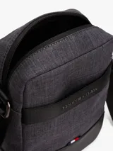 Bandolera Tommy Hilfiger modelo TH Melange Mini Reporter, color gris oscuro con detalles en negro. Presenta una franja horizontal con el logo de la marca y el detalle de la bandera en la parte inferior.