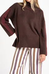 Sweater de punto color marrón oscuro jaspeado, con cuello alto y mangas largas. Presenta una franja vertical de tejido acanalado en color bordó en la parte superior de ambas mangas y un ribete bordó en el cuello.