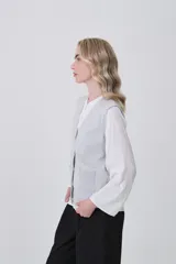 Chaleco de punto color crema, con cuello en V, cierre frontal de botones y dos bolsillos frontales.