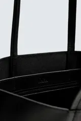 Bolso tipo shopper fabricado en cuero negro. Tiene un bolsillo interior plano con cierre mediante cremallera y asas de cuero.
