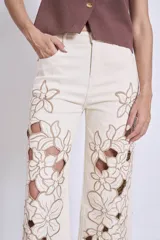 Pantalón de jean color crudo con bordados florales y aberturas en las piernas.