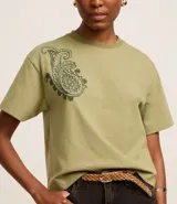 Remera boxy de algodón color verde oliva, con cuello redondo y mangas cortas. Presenta un bordado paisley en el hombro izquierdo.