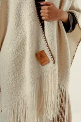Ruana tejida a mano en lana merino 100%, de color marrón con detalles de costura en rojo en los bordes y terminación de flecos largos en el ruedo. Presenta una silueta amplia y caída natural, confeccionada artesanalmente por Manos del Uruguay.