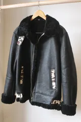 Campera bomber de cuero negro con interior de piel sintética color crema. Presenta cierre frontal, cuello y puños de piel sintética y apliques de cuero con estampado animal print.