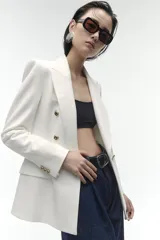 Blazer color blanco hueso, de corte entallado y doble botonadura dorada.