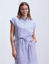 Vestido camisero corto con estampado de rayas verticales celestes y blancas. Tiene cuello camisero, mangas cortas con dobladillo, cierre frontal con botones y cinturón de lazo en la cintura.