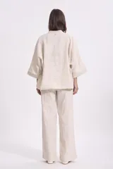Blusa color crema de lino, de corte holgado, con cuello en V, mangas anchas y un botón grande negro.