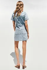 Vestido corto de denim azul, con cuello solapa, escote en V, manga corta, bolsillos delanteros y cierre frontal con botones metálicos.