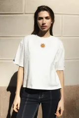 Remera blanca de algodón con cuello redondo y mangas cortas. Presenta un bordado del sol de la bandera uruguaya en el pecho.