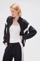 Campera deportiva negra con cierre frontal, cuello alto y detalles de recortes curvos blancos en mangas y laterales.