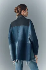 Campera oversize de denim rígido con parches en distintos tonos de azul y negro. Cierre frontal con botones metálicos con logo de marca y bolsillos en el frente.