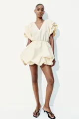 Vestido corto color crema con escote en V pronunciado, mangas globo cortas con diseño raglán, costura elástica en la cintura y pollera globo con volumen.