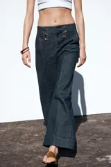 Pantalón culotte de tiro alto en denim azul oscuro, con pernera ancha y corta terminada en vuelta. Presenta falsos botones dorados en la parte delantera, bolsillos frontales y cierre con cremallera y gancho.