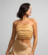Blusa cropped color beige de satén con escote strapless, diseño con pliegues horizontales y cierre lateral con cremallera invisible.