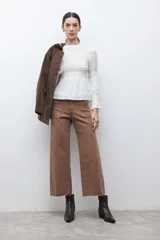 Blusa de color crudo con cuello alto fruncido y pechera con nido de abeja. Cuenta con mangas largas con detalles elásticos y puños con volados, y un bajo de corte peplum.