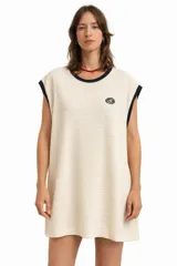 Vestido corto de tejido tipo waffle color crema, sin mangas, con cuello redondo ribeteado en azul marino y un pequeño logo bordado en el pecho.