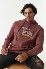 Canguro de felpa color ladrillo con capucha y cordones ajustables. Estampado frontal con la frase "Regret nothing" y logo de la marca Mistral.