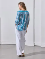 Blusa de gasa estampada con rayas verticales en tonos celeste, azul y blanco. Tiene cuello a la base con escote en V y abertura con botones. Las mangas largas son de largo regulable.