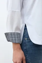 Remera blanca de manga larga con puños doblados que muestran un estampado vichy (cuadros) en azul marino y blanco. Tiene cuello redondo y un calce relajado.