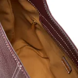 Bolso tipo hobo de cuero sintético (PU) color bordó, con costuras blancas visibles en el centro. Posee un asa corta fija y una correa larga desmontable y regulable con tejido a rayas blancas y negras. Cuenta con cierre metálico superior y herrajes dorados.