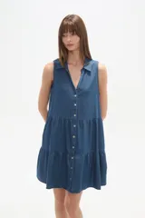 Vestido gris de algodón, largo hasta la rodilla, con cuello camisero, sin mangas, cierre frontal de botones blancos y falda con volados.