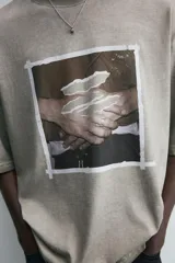 Camiseta color caqui con estampado de manos en el frente, corte holgado, cuello redondo y mangas cortas.