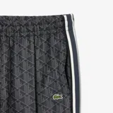 Pantalón de jogging negro con estampado de monogramas geométricos en gris y blanco. Tiene corte recto, cintura con cordón ajustable, bolsillos laterales y logo de cocodrilo bordado en el muslo.