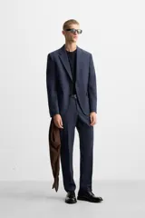 Blazer azul marino con sutil diseño de cuadros, corte regular fit, cuello con solapas de muesca, manga larga con puños abotonados, bolsillo de vivo en el pecho, bolsillos de solapa en la cadera, bolsillo interior, aberturas en la espalda y cierre frontal con dos botones.