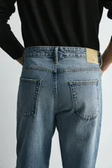 Jeans de denim de algodón, color negro lavado, con tiro medio, corte ajustado en cadera y muslos, y pierna que se estrecha hacia el tobillo. Presenta cinco bolsillos y cierre frontal con cremallera y botón.