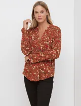 Blusa de manga larga color marrón terracota con estampado floral en tonos rojos, blancos y verdes. Presenta un escote en V con cuello mao y mangas que se pueden ajustar con presilla y botón.