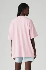 Remera rosa de corte holgado con estampado de texto e imagen abstracta en el frente.