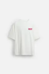 Camiseta blanca de corte relajado, con cuello redondo y mangas cortas. Presenta estampados combinados en contraste en la parte delantera y trasera con la frase "Gourmet Groove LLC".