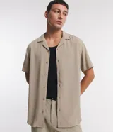 Camisa boxy masculina de viscosa color beige, con mangas cortas, cuello camisero y abotonadura frontal.