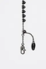 Pulsera de acero inoxidable en color negro con una hilera de pequeños cristales facetados en forma de corazón. Cuenta con un cierre de mosquetón y una cadena de extensión ajustable para adaptarse a la muñeca.