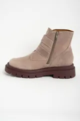 Bota corta de cuero color rosa viejo o beige claro, con suela track gruesa color marrón oscuro. Presenta dos tiras ajustables con hebillas metálicas color bronce y cierre lateral.