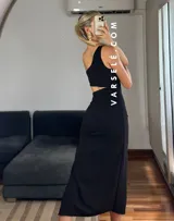 Vestido midi negro con corte asimétrico, una manga, abertura lateral y frunce en la cintura.