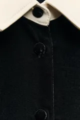 Camisa negra de terciopelo con cuello solapa, manga larga con puños en tejido color crema a contraste y bajo redondeado.