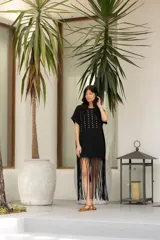 Vestido negro de algodón con corte recto, cuello redondo, mangas cortas, tachas plateadas en el frente y flecos largos en el ruedo.