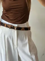 Cinturón marrón con estampado animal print de vaca, hebilla metálica plateada y trabilla a tono.