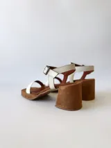 Sandalias de cuero color crudo, con dos tiras anchas sobre el empeine, pulsera al tobillo con hebilla y taco cuadrado de madera.