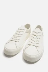 Zapatillas deportivas blancas con detalle de color a contraste en el talón y suela con acabado irregular.