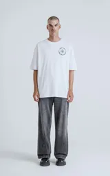 Remera blanca de manga corta con cuello redondo y calce oversize. Presenta una estampa en sublimación inspirada en el tarot, con la imagen de una figura femenina sosteniendo un salvavidas con la frase "Chill Bitch Trust Karma" y el texto "The Wheel of Fortune" en la parte inferior.