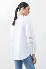 Camisa blanca de manga larga con detalles de encaje en el frente y las mangas.