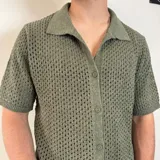 Camisa tejida de manga corta color verde oliva, con cuello tipo polo y cierre frontal con botones.