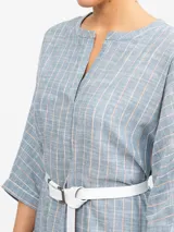Túnica midi de lino color crudo con finas rayas verticales en tono marrón. Presenta cuello en V con abertura y mangas tres cuartos. La cintura se ajusta con un lazo del mismo tejido, y tiene aberturas laterales en el ruedo.