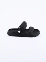 Sandalia tipo 'slide' de goma, color negro, con dos tiras anchas y acolchadas sobre el empeine, ajustables mediante un broche blanco en el lateral.