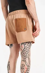 Short de baño de calce regular, color camel (marrón claro), con paneles de tela en tono marrón más oscuro en los bolsillos cargo laterales y en la parte superior de los bolsillos delanteros. Posee cintura elástica con cordón negro estampado.