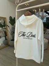 Hoodie negro de corte oversize, con capucha, bolsillo frontal y estampado blanco en la espalda con la inscripción "The Dolls The Dolls VIP CLUB".