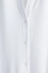 Camisa blanca de viscosa con efecto arrugado, de manga corta, corte holgado, cuello clásico, botones frontales y canesú con pliegue de caja en la espalda.