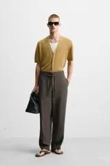 Pantalón marrón oscuro de corte amplio, con cintura ajustable con cordón, bolsillos plastrón delanteros y traseros, detalle de costuras frontales y cierre frontal con cremallera y gancho metálico oculto.